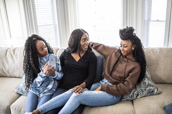 Mother talking with teenage daughters on sofa