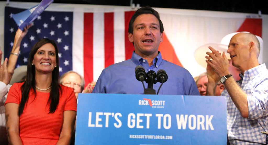 Florida governor Ron DeSantis stands in front of an American flag as he gives a speech at a podium.