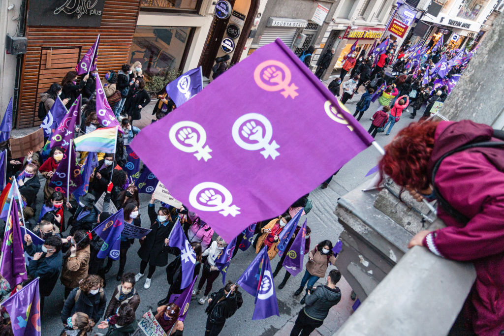 Protesters are seen walking while holding feminist flags.