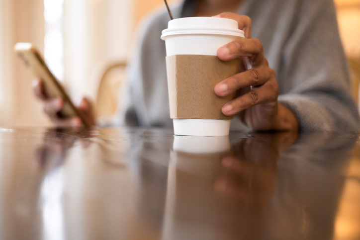 black woman enjoys morning coffee in disposable cup while using smart phone