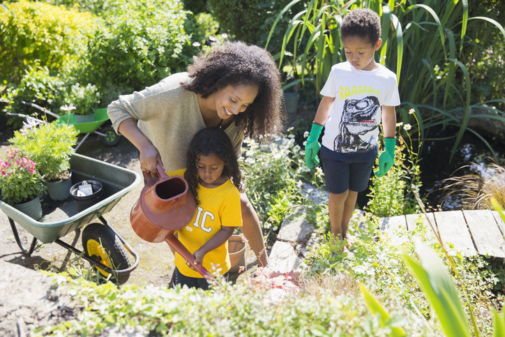 Happy mother and children watering plants in sunny summer garden