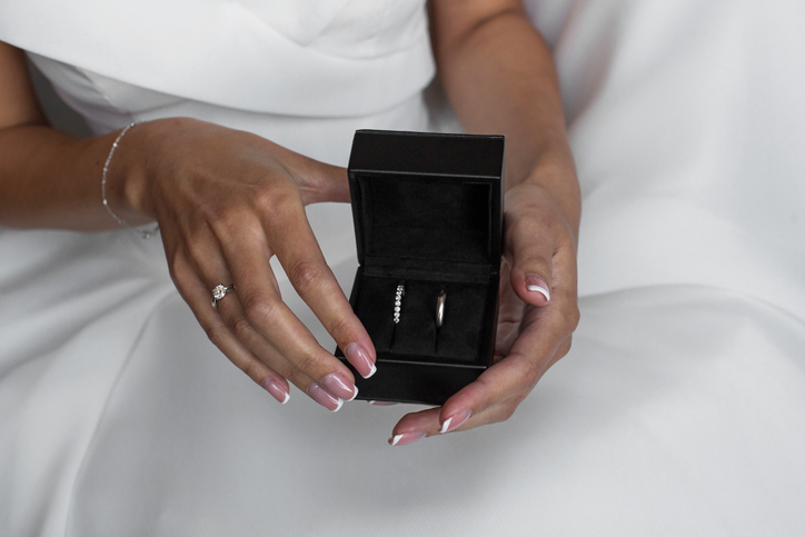 Close-up view of bride in white dress holding black box with wedding rings.