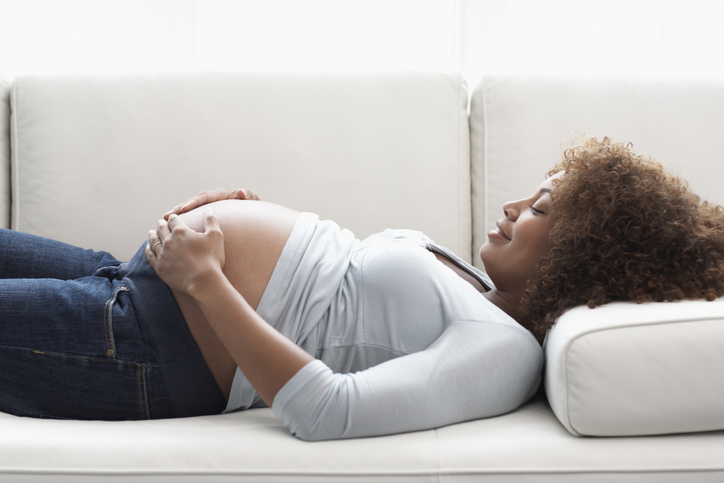 Maternity, Pregnant Woman Holding Stomach on Sofa