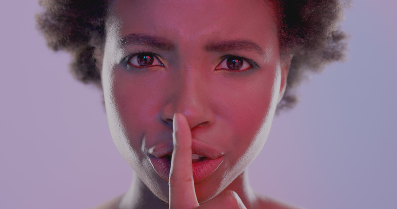 Studio shot of a young woman posing with her finger over her lips against a pink background