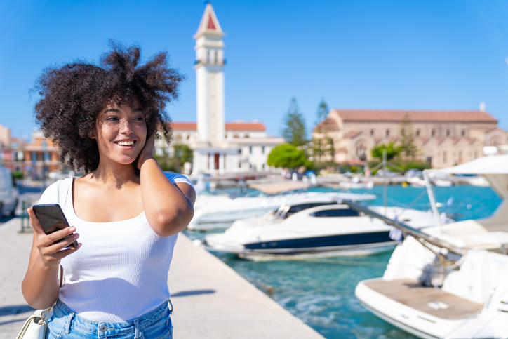Afro woman enjoying vacations in Zakynthos Greece and using smart phone