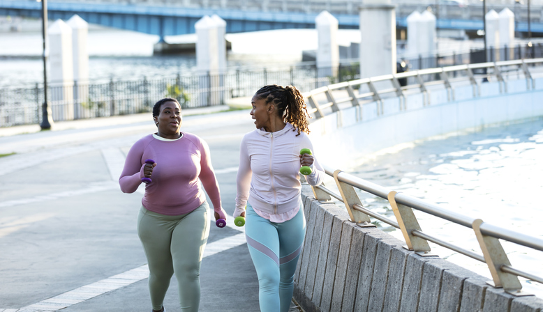 Two African-American woman running together in city park