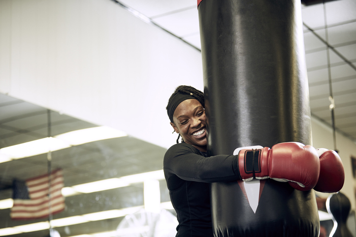 Happy female boxer holding punching bag at health club