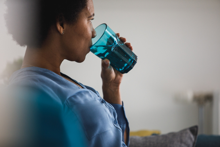 Copy space shot of mid adult woman sipping water from a blue drinking glass