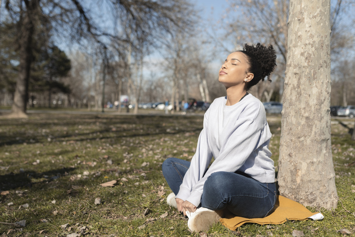 Portrait of a young Afro woman enjoying meditating in the park