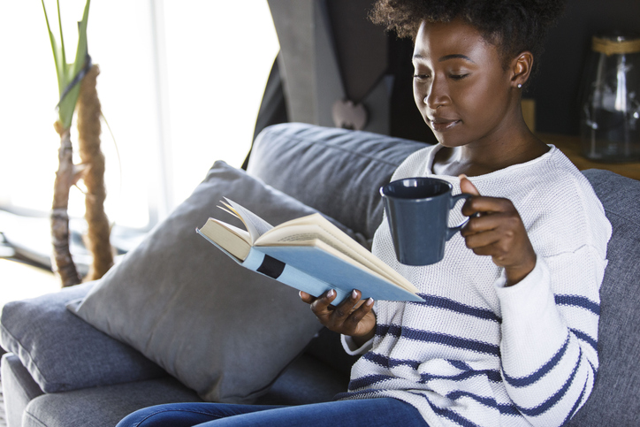 Joyful young woman reading a book while enjoying morning coffee