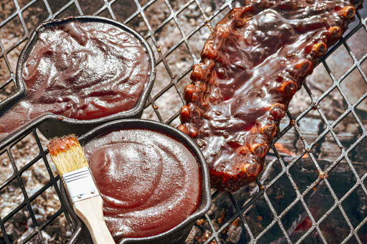 Baby Back Pork Ribs And Cast Iron Pots Full Of Barbecue Sauce On Grill