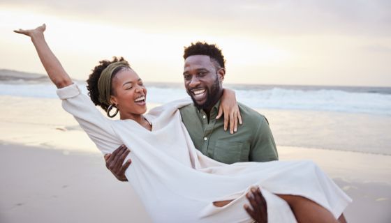 Laughing young couple having fun together on a beach at sunset