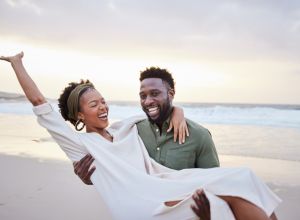 Laughing young couple having fun together on a beach at sunset