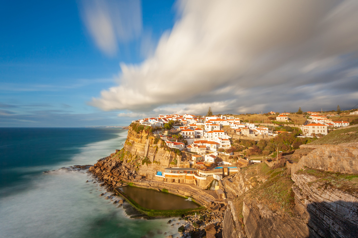 Picturesque village Azenhas do Mar. Holiday white houses on the edge of a cliff with a beach and swimming pool below. Landmark near Lisbon, Portugal, Europe. Landscape at sunset.