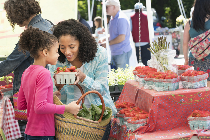 Black mother and daughter smelling strawberries at farmers market