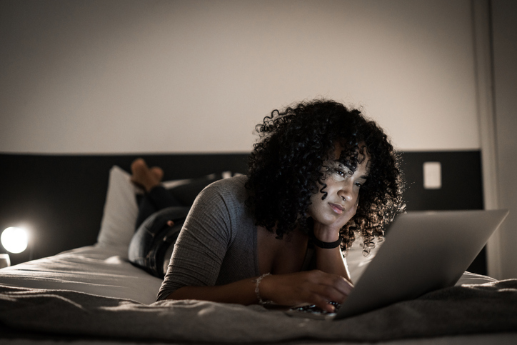 Tired young woman lying in bed using laptop at home