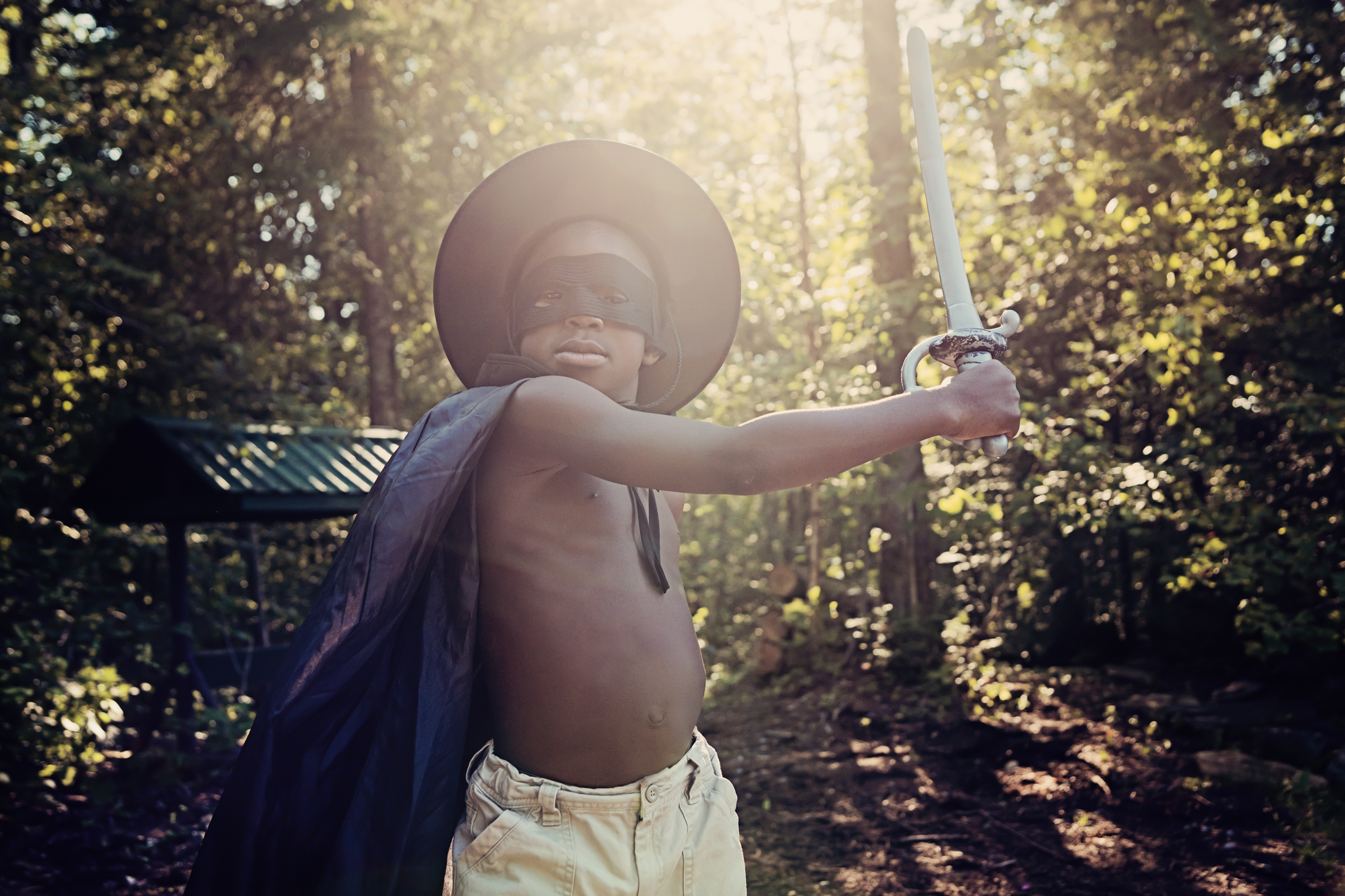 Little black boy costumed as Zorro playing outside.