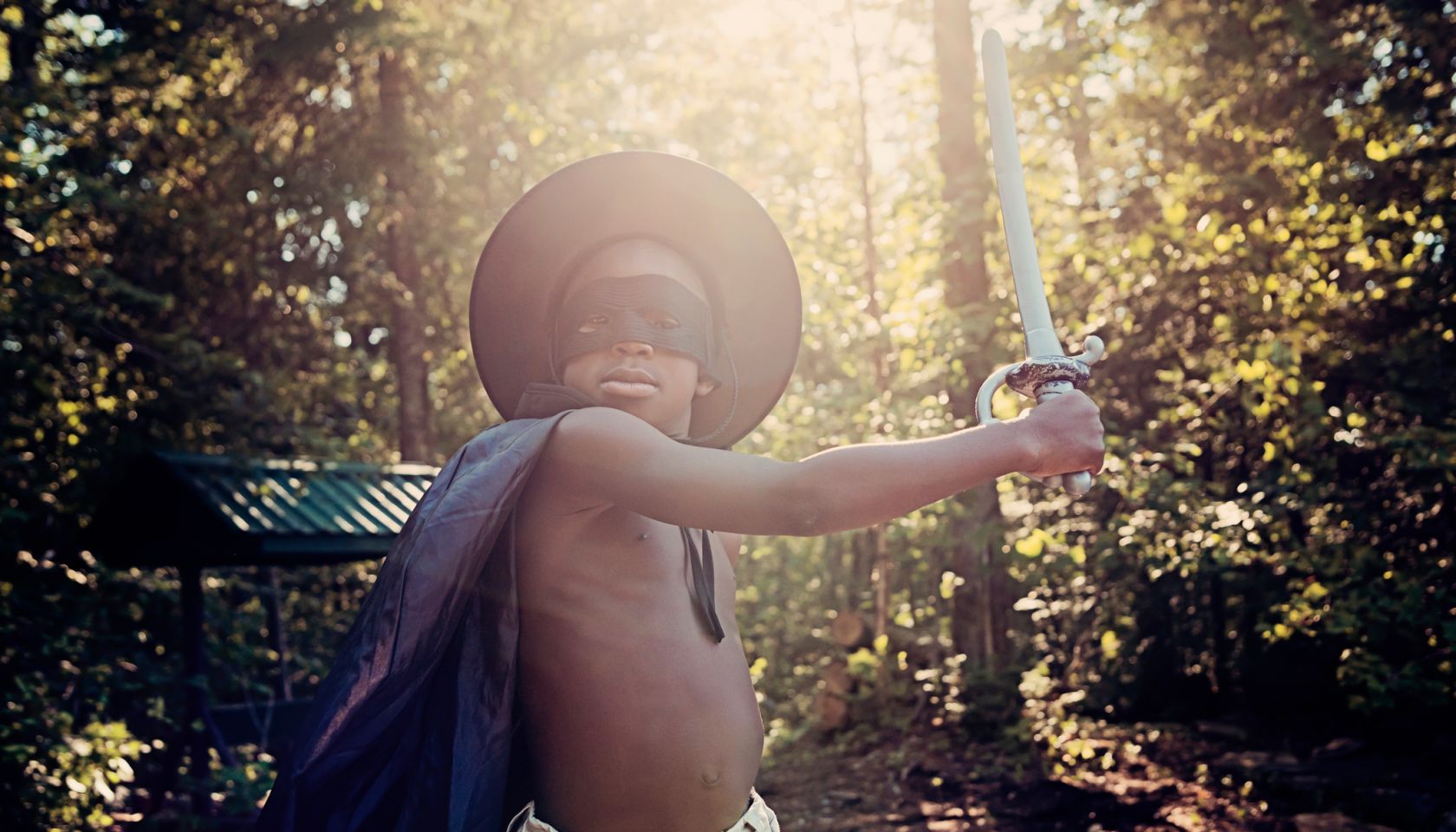 Little black boy costumed as Zorro playing outside.