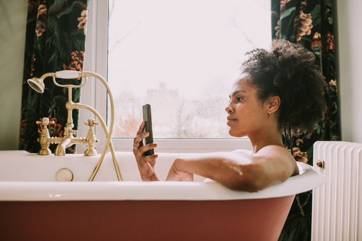 A woman uses a mobile phone while relaxing in a bath considering social media and mental health