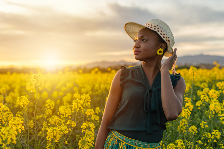 Portrait of beautiful african american woman enjoys summer and life outdoors in countryside yellow flowers field at sunset
