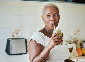 Young African woman drinking on a smoothie with a reusable straw trying internal shower trend