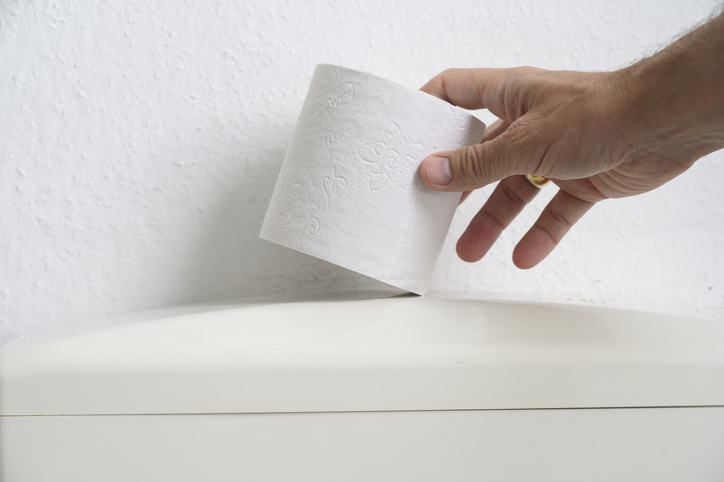 Man's hand catching toilet paper on a toilet.