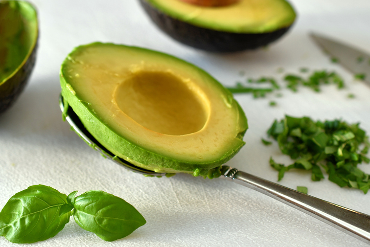 Prepare an avocado and herbs, basil and chives, to cook with them on a white cutting board.