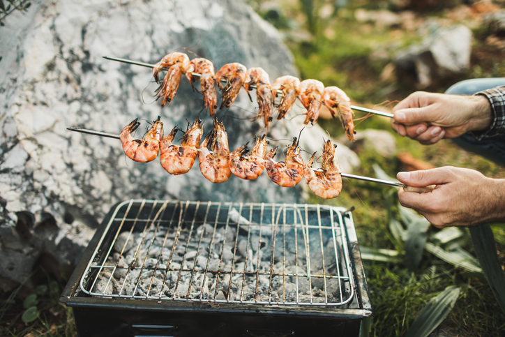 Close-up of man's hands cooking grilled shrimp on barbecue.