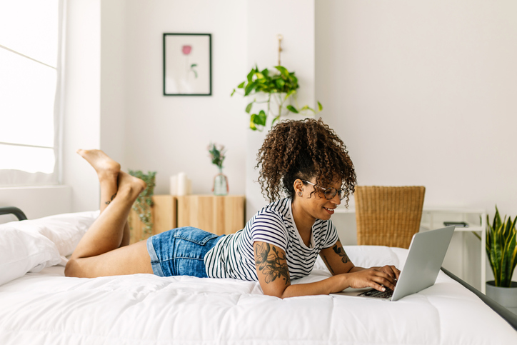 Happy woman using laptop lying on bed