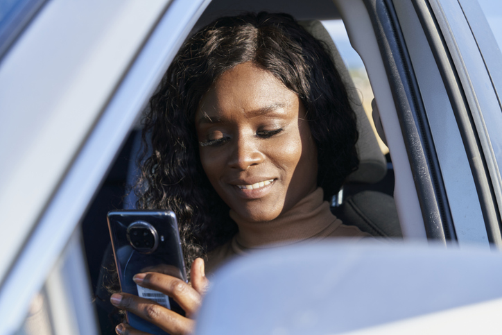 Happy woman black hair using smart phone relaxing while traveling by a car