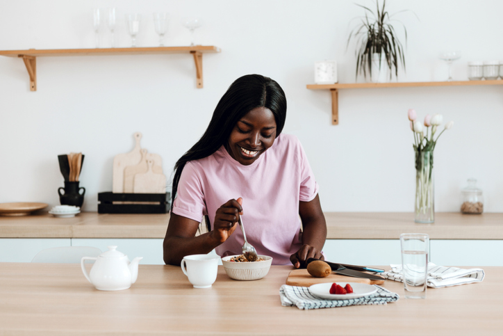 Smiling black woman using smart phone during her breakfast at home.