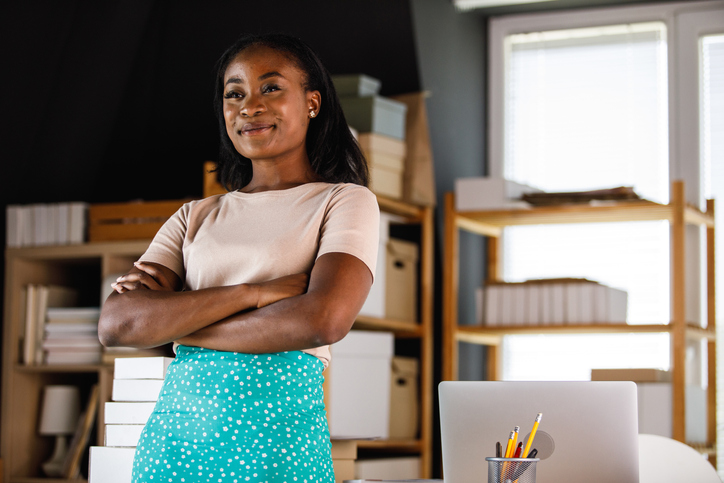 Confident businesswoman standing by her desk, arms crossed, smiling