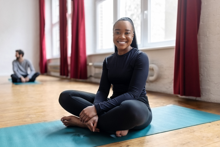 African woman yoga teacher sitting on fitness mat in class