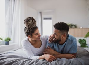 Portrait of young couple on bed indoors at home, looking at each other.