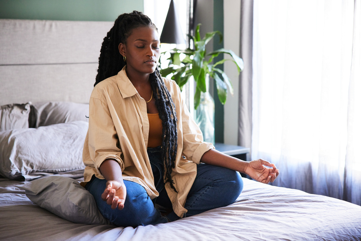Young woman sitting on her bed and meditating in the morning