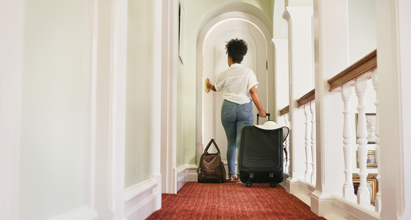 Rearview shot of an unrecognizable young woman walking into a hotel room with her luggage in tow