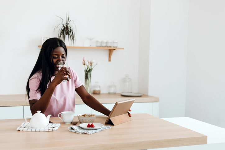 Smiling black woman using digital tablet during her breakfast at home.