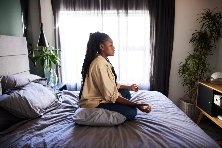 Young woman meditating on her bed at home in the morning