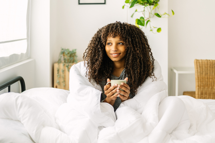 Portrait of young afro american woman drinking coffee while sitting on bed in the morning