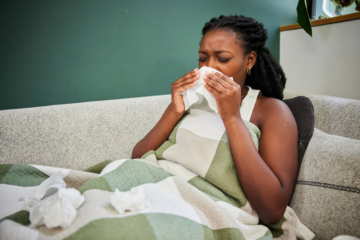 Young woman sneezing into tissue while lying sick on her sofa