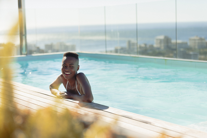 Happy young woman in sunny, luxury swimming pool