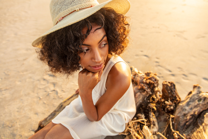 African American girl in hat sitting on driftwood