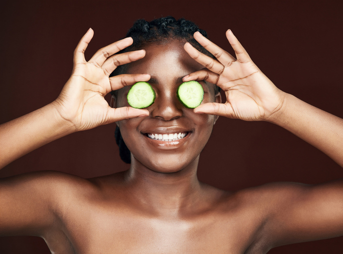Studio shot of an attractive young woman covering her eyes with cucumber against a brown background
