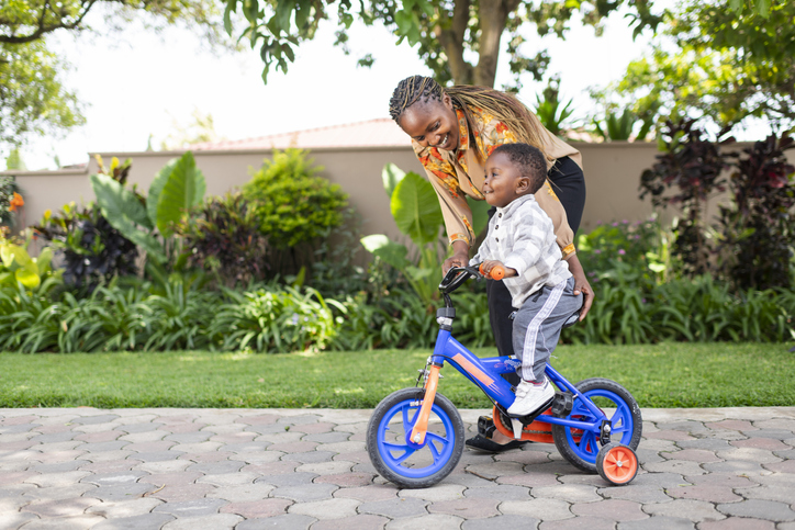 Toddler having fun on bicycle with mother at home