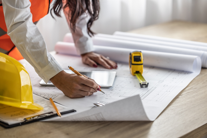 Female civil engineer notes changes on blueprints by a pencil.