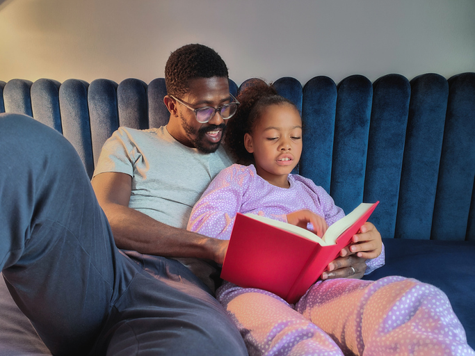 Black Father and Mixed-Race Daughter Reading A Story in Bed