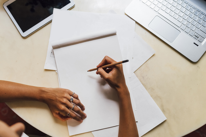 Hand of fashion designer holding pencil on sketch pad at desk