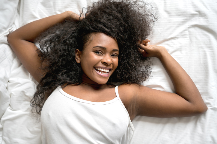 Portrait of a beautiful latin american black woman relaxing on her bed stretching her arms and looking at camera smiling