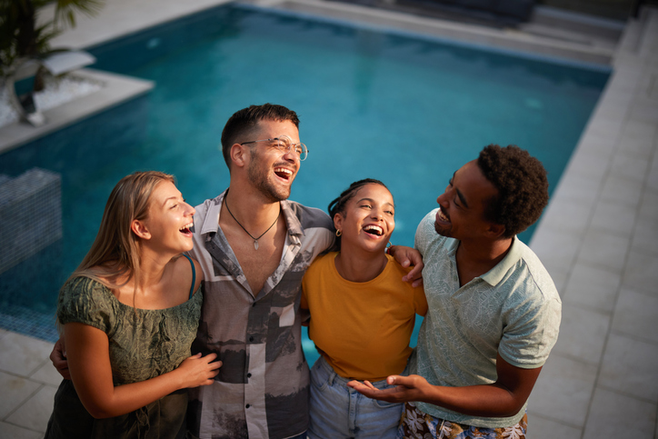 Group of young cheerful friends talking by the pool.