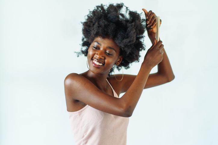 Smiling multiracial woman combing her black curly hair, neutral background.